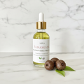 Organic Tamanu Oil bottle with tamanu nuts and green leaves on marble background